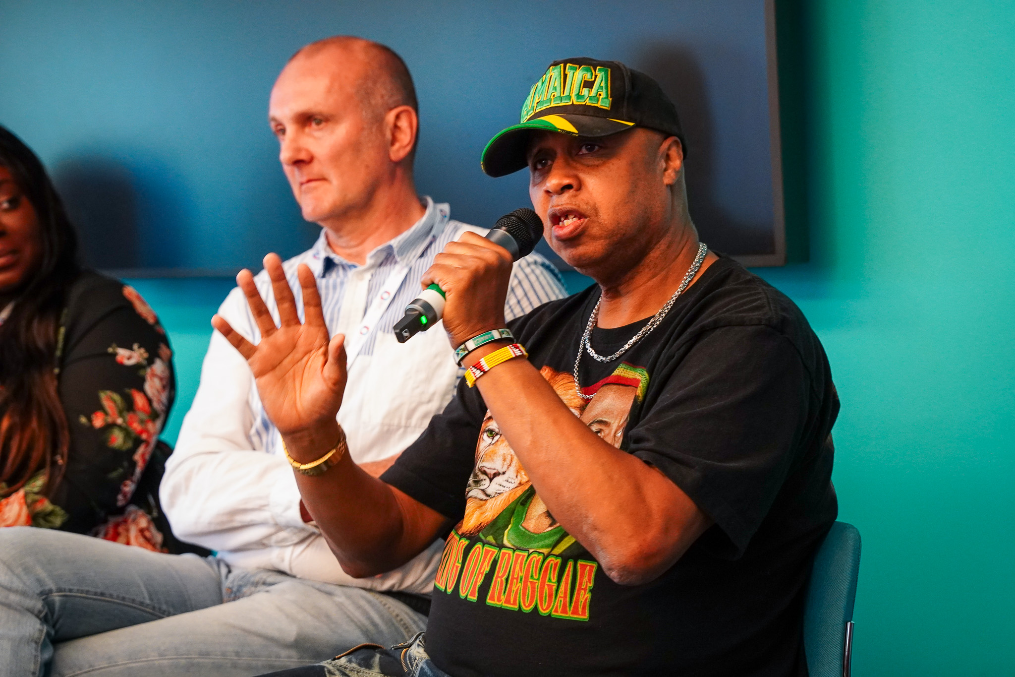 A man wearing a cap holds a microphone and speaks