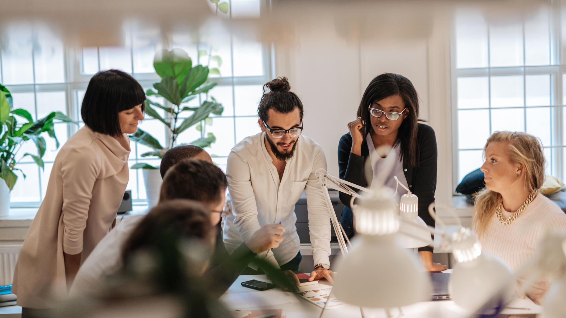 A group of people clustered around a table discussing something. They are concentrating while a man and woman lead the conversation.