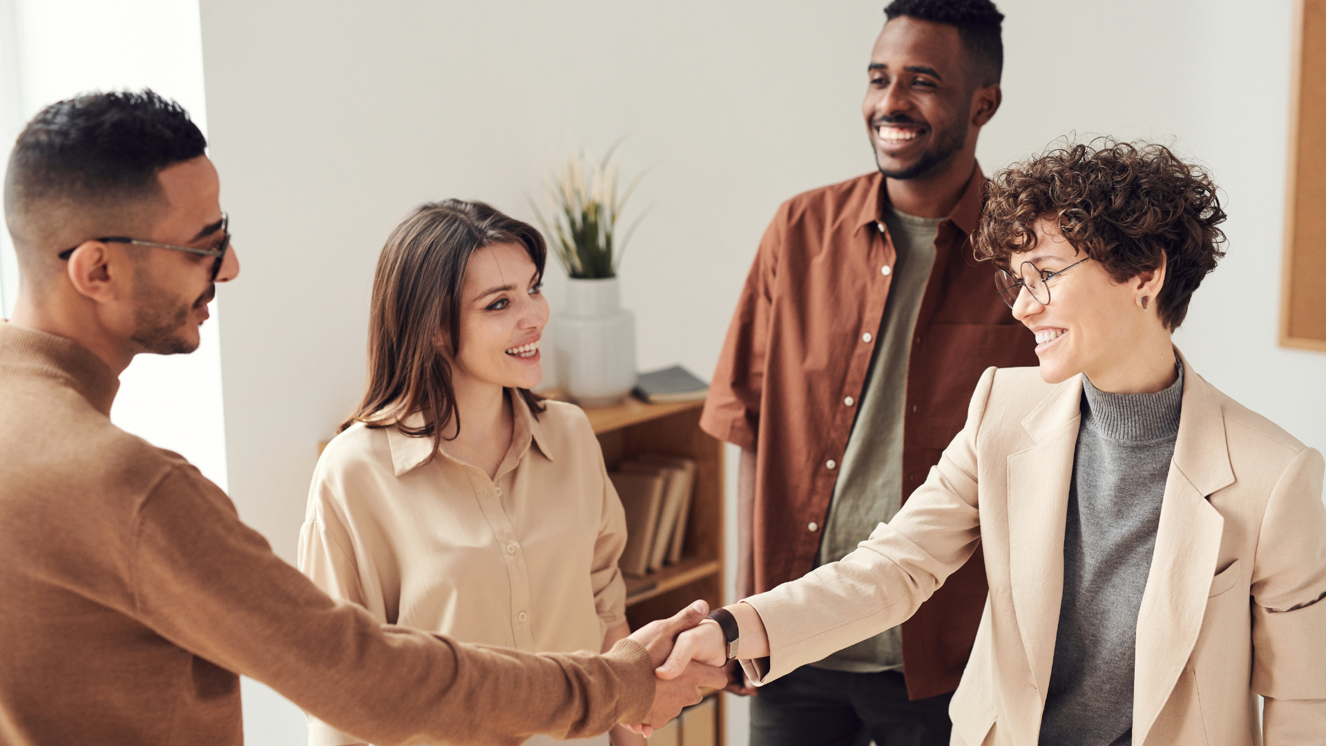 A group of 4 people, all smiling while 2 shake hands