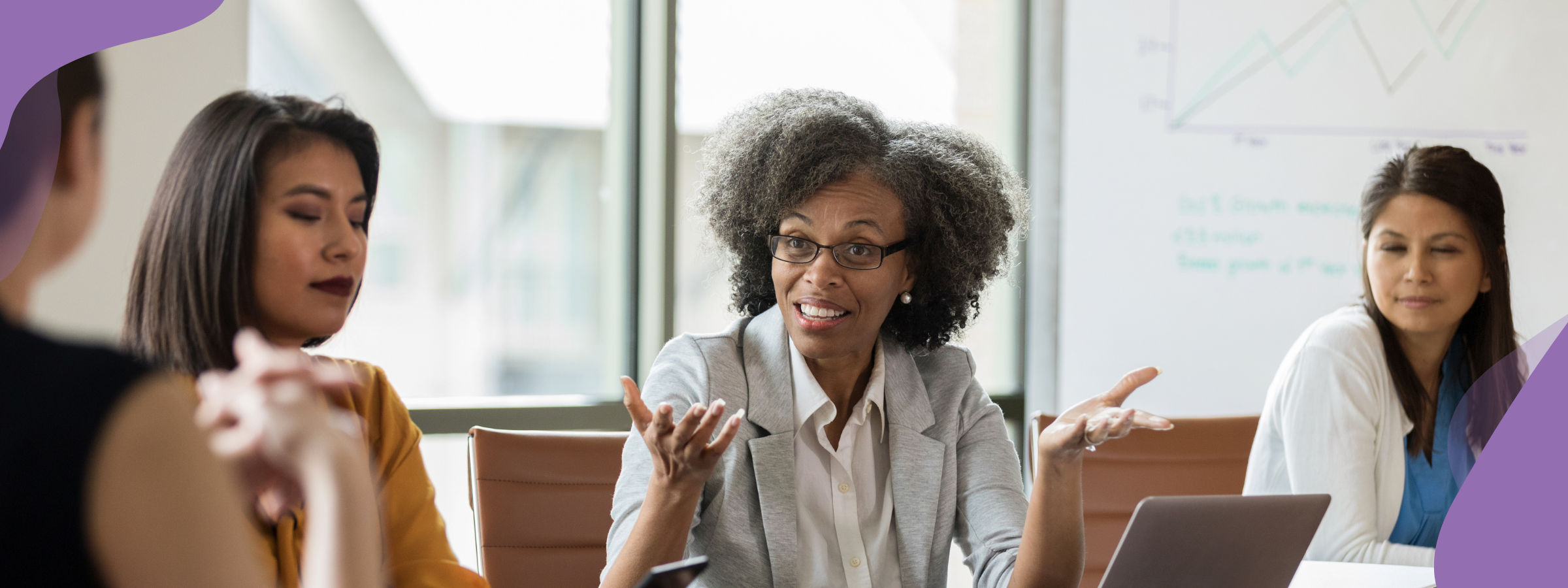 A group of women at a table in conversation. One woman is gesturing as if to ask a question.