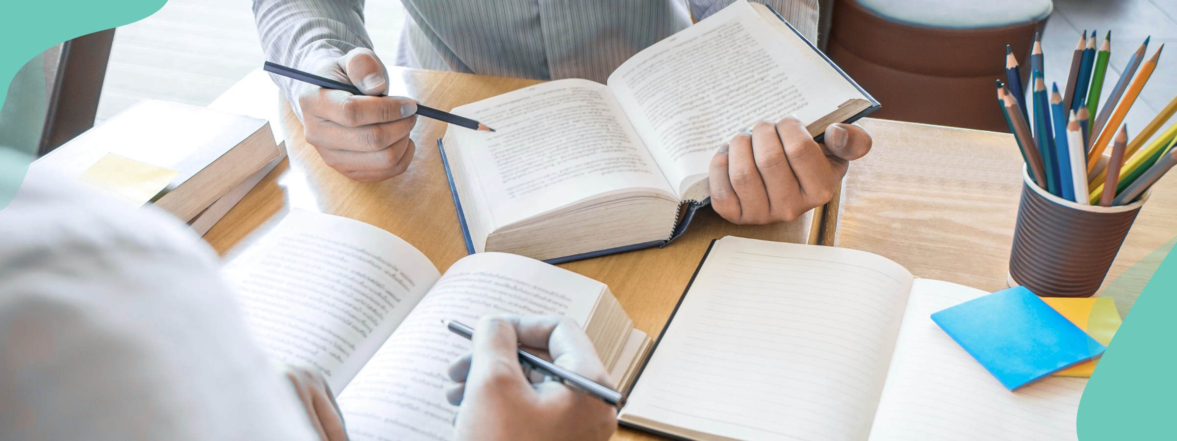 Image focuses on books held by two people at a table