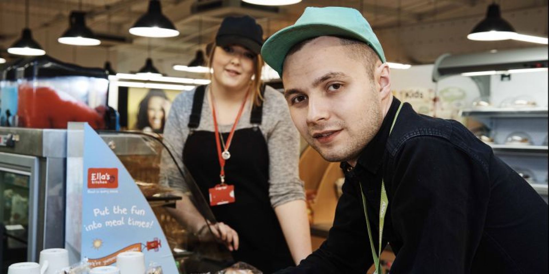 A woman wearing a black hat and apron and a man wearing a black shirt and a green hat. They're both looking toward the camera.