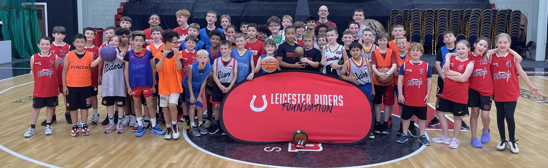 Group of young children from Leicester Riders Foundation standing together collecting a sports award in a basketball court