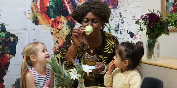 Woman drinks from pretend tea cup with two children