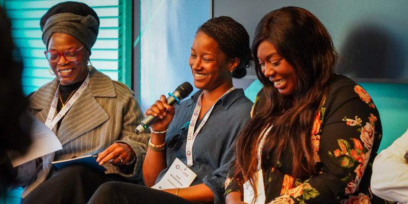 A panel of women smiling and holding a microphone