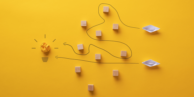 A conceptual image of 2 routes towards a lightbulb - one straightforward and one with square obstacles in the way, a line indicating a more convoluted path