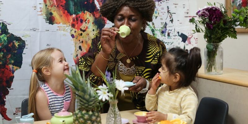 Woman drinks from pretend tea cup with two children