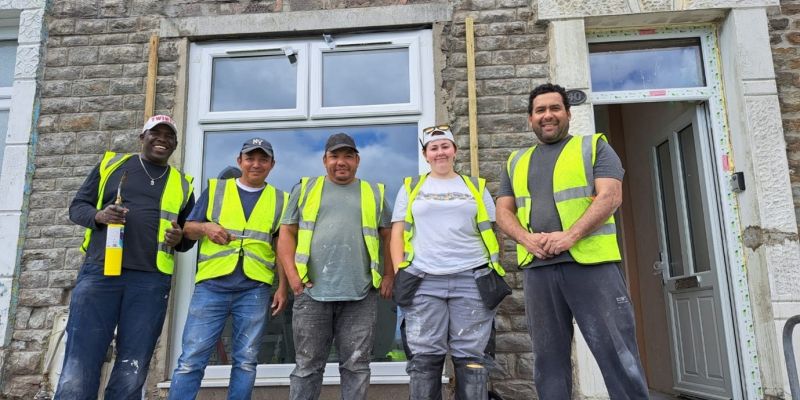 5 men wearing Hi-vis vests outside a building smiling.