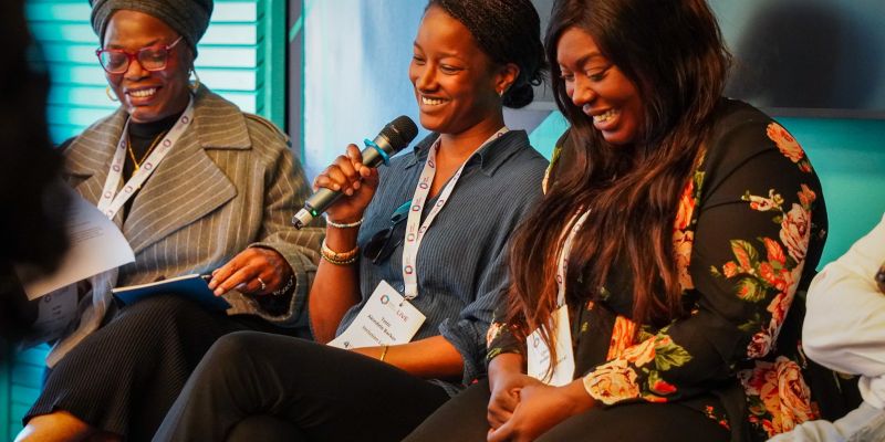 A panel of women smiling and holding a microphone