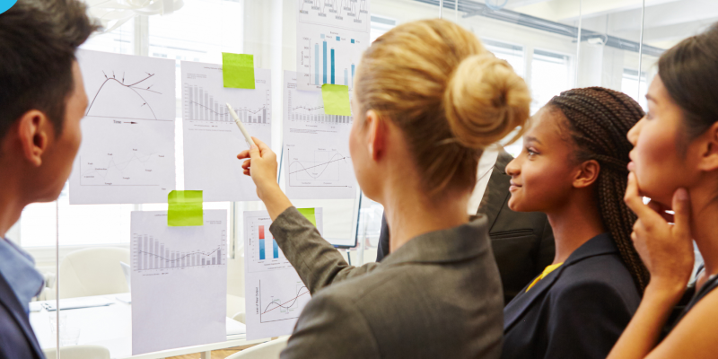 A group of professionals looking at graphs and reports on a board