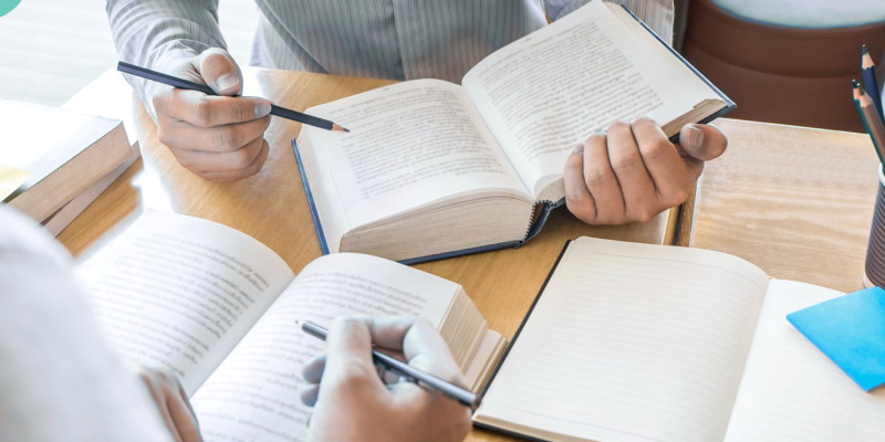 Image focuses on books held by two people at a table